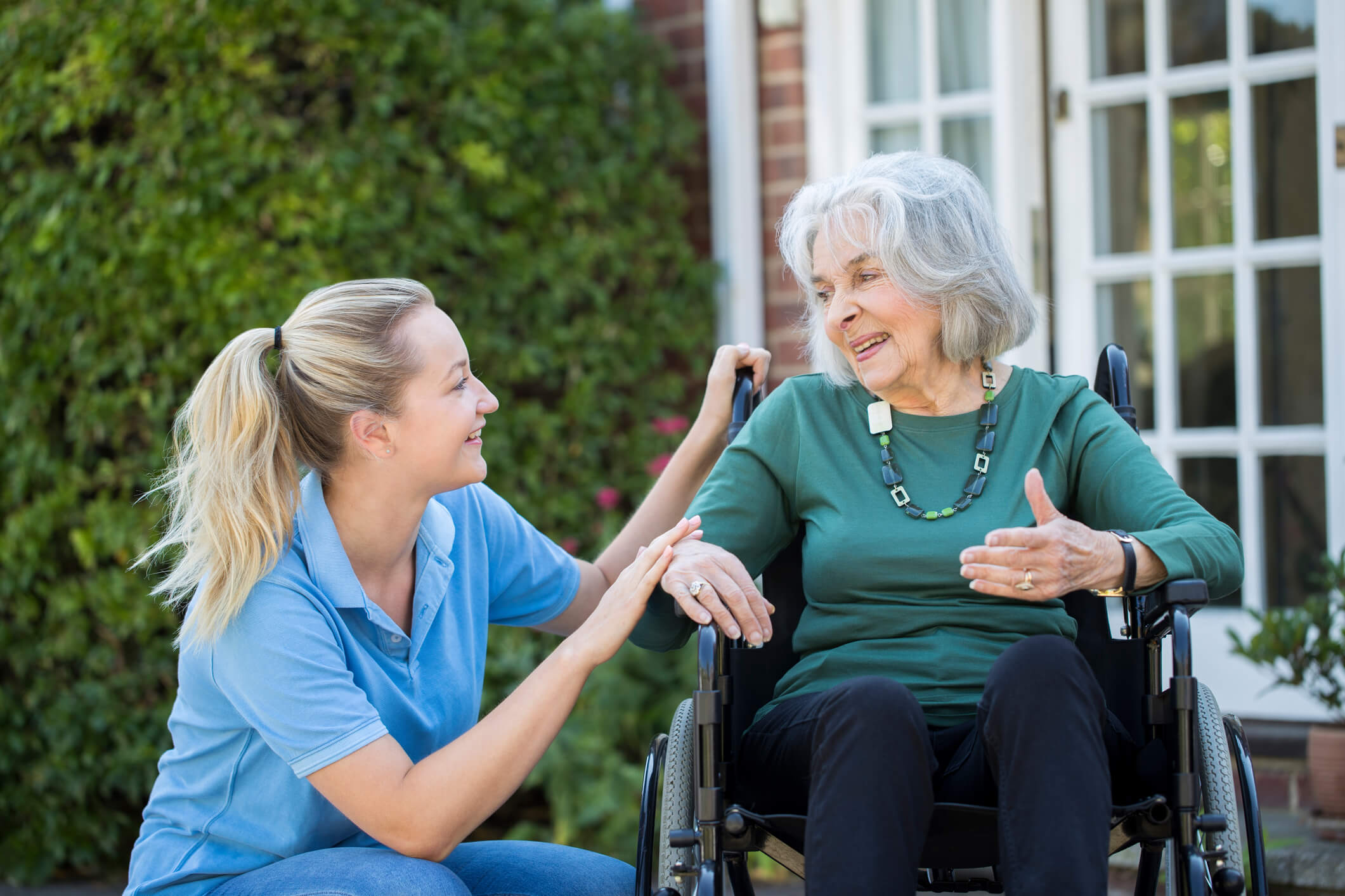Carer smiling with an older woman in a wheelchair