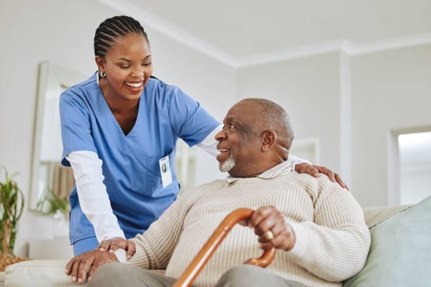 Carer supporting a man sitting on a sofa with a walking stick